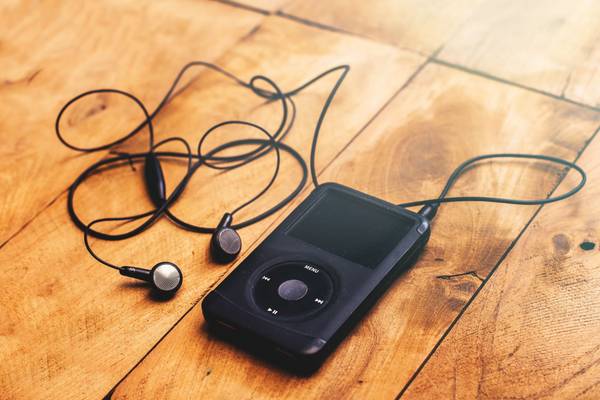 Close up on iPod classic 120 GB in black case with headphone on a wooden table background.