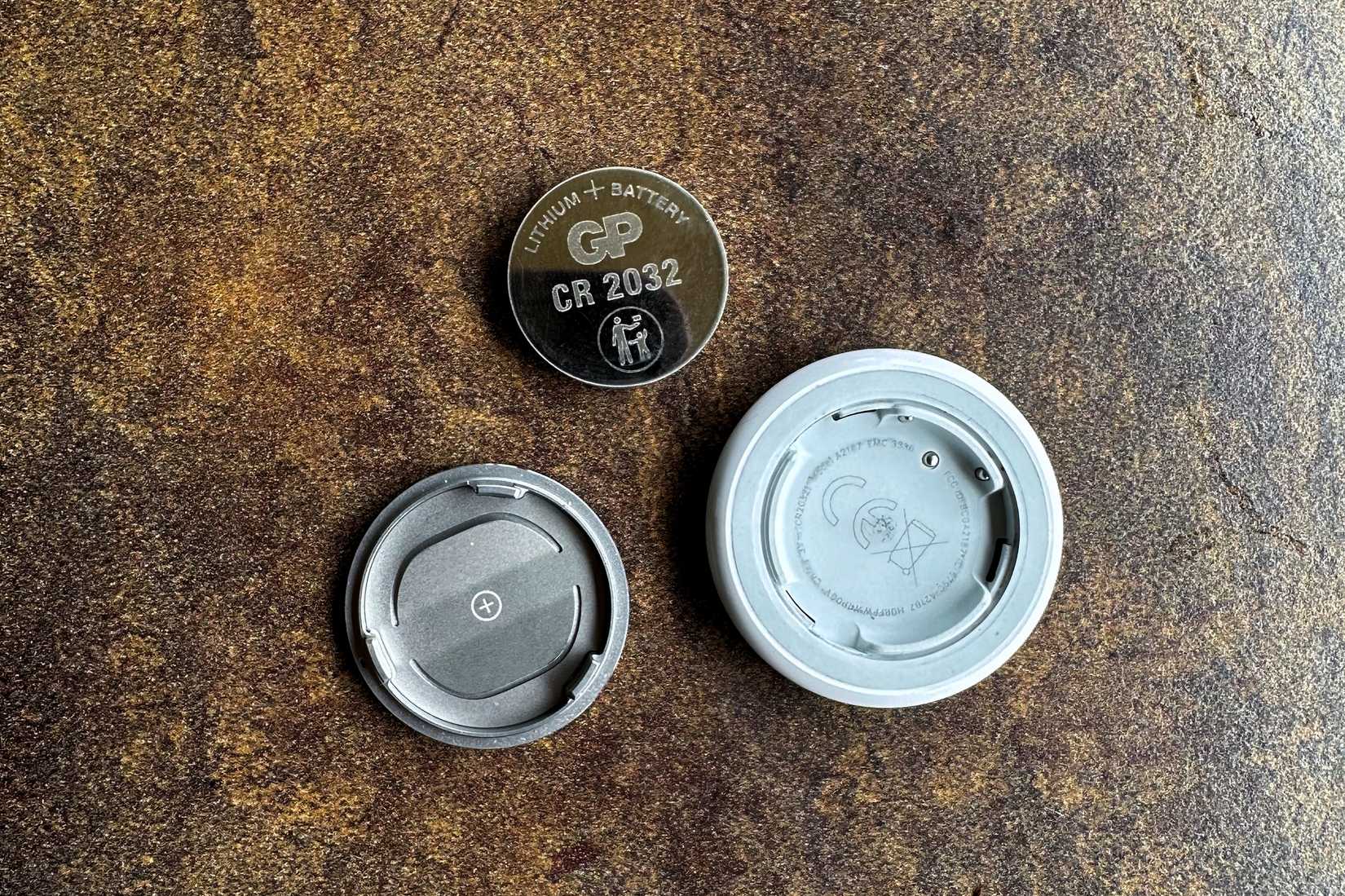 Apple AirTag on a wooden table with its back cover open and the internal battery taken out.