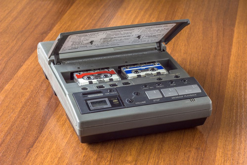 Old vintage answering machine with two small tape cassettes on a wooden table surface.