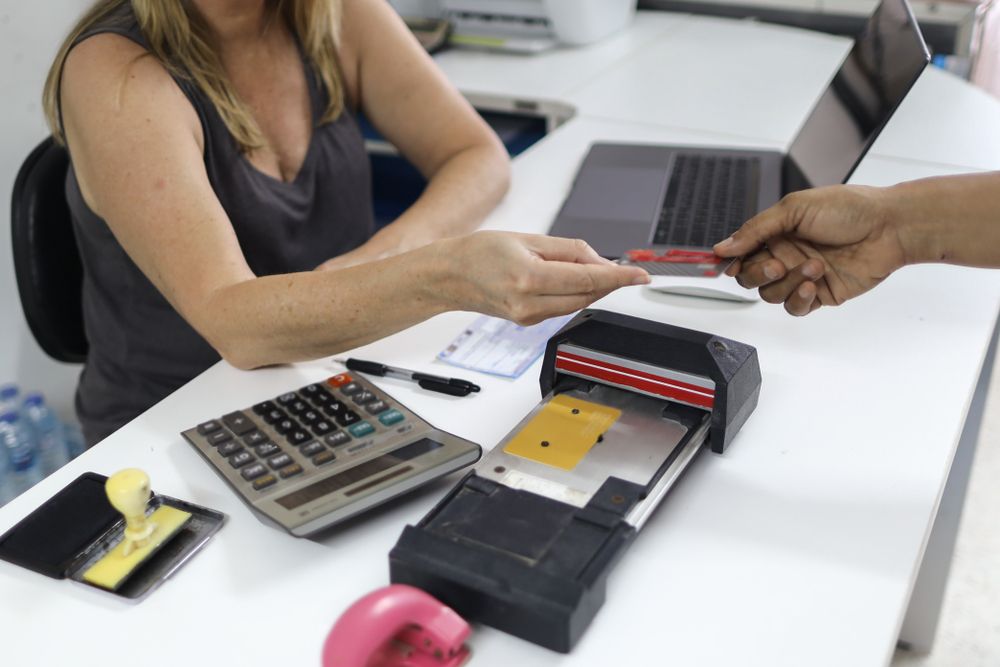  Old credit card imprinter machine on the white table with offices.