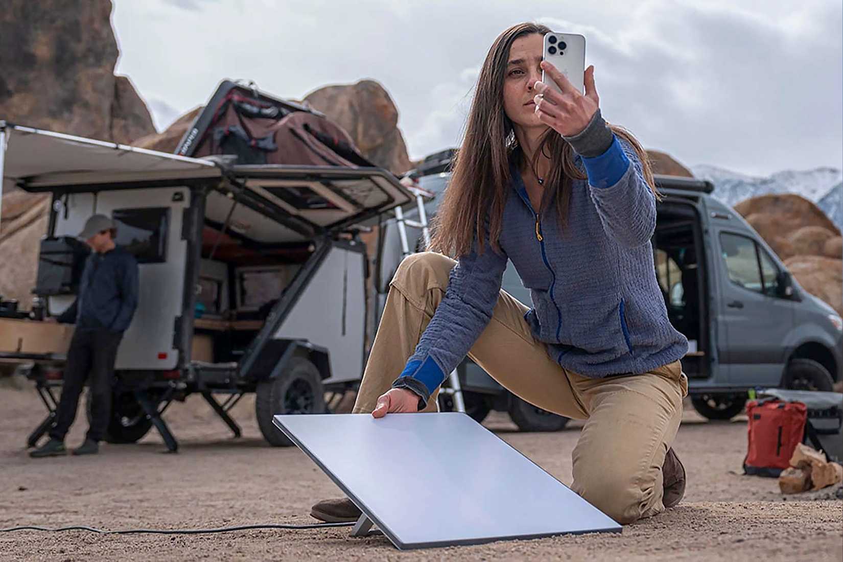 A woman sets up a Starlink Mini in a remote desert near a truck.