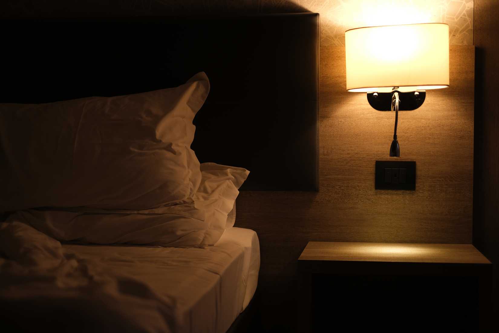 Beside lamp emitting soft, warm light on the bed.