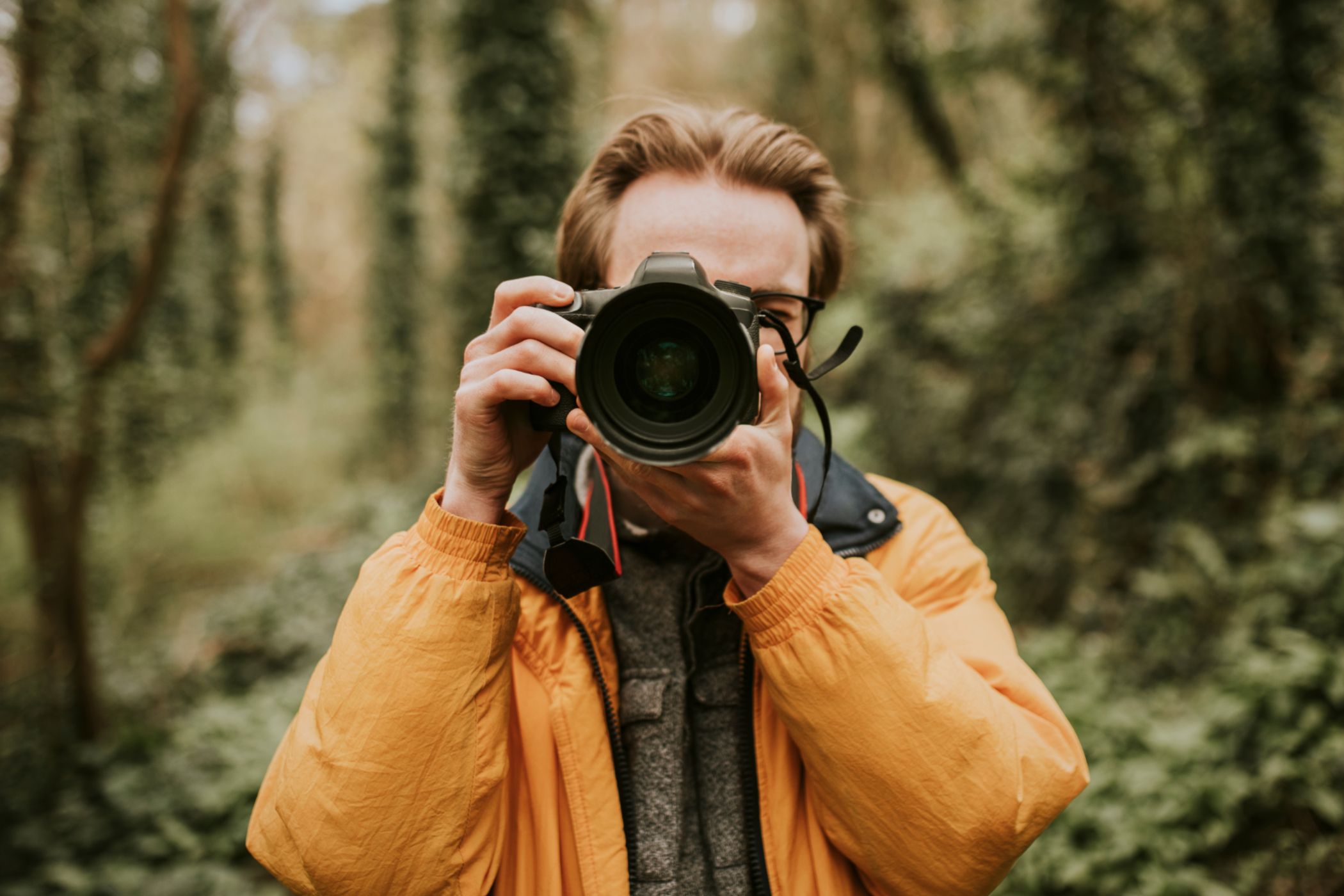 Male photographer in the forest pointing a camera.