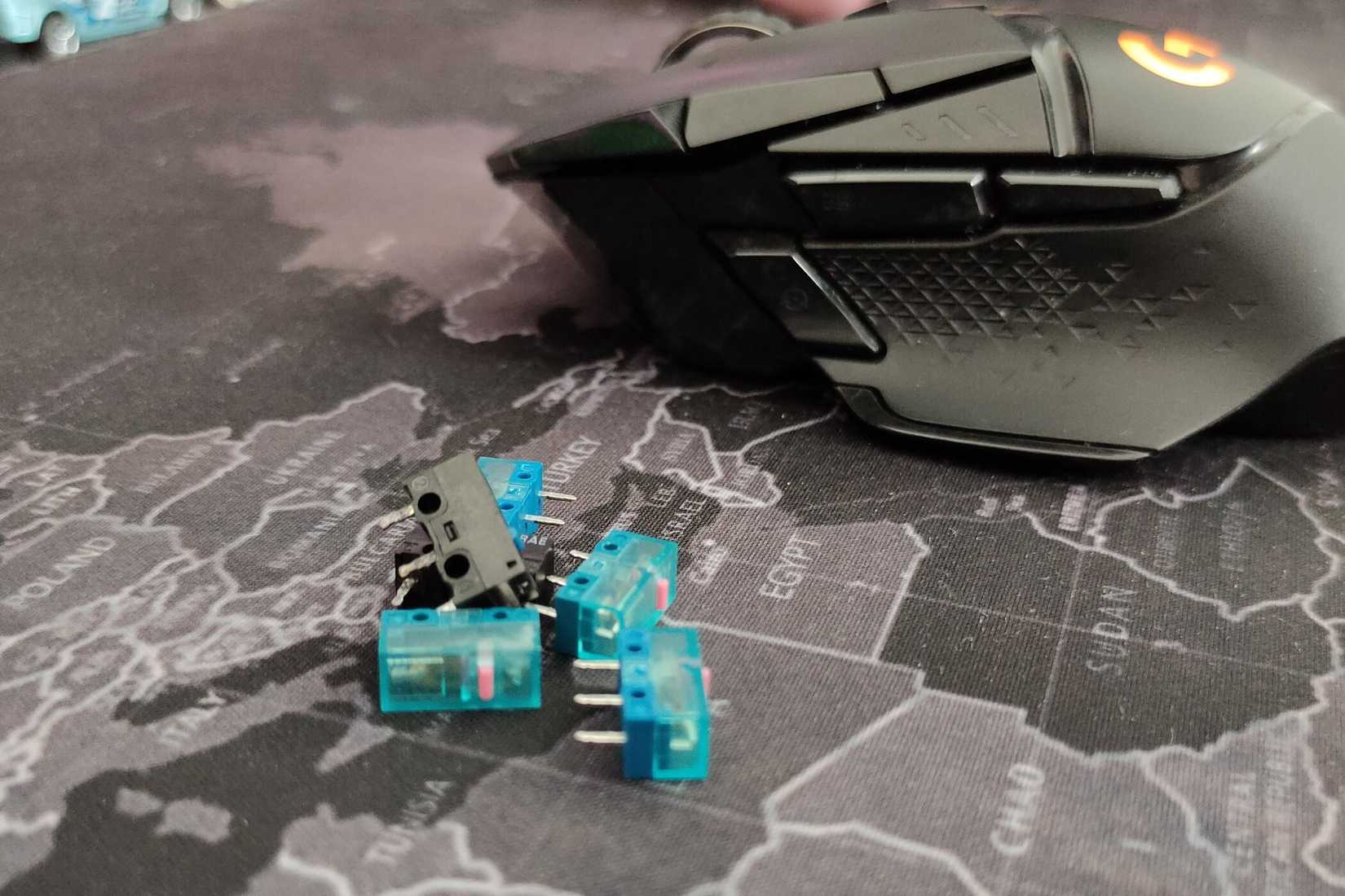 A set of Huano and Omron precision mouse switches on the mouse pad next to the Logitech G502 gaming mouse.