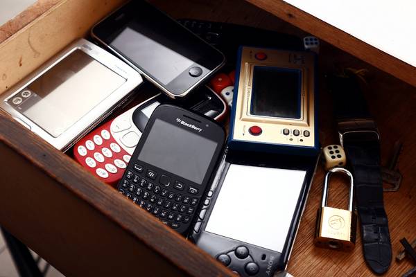 A desk drawer full of old phones and handheld game consoles.