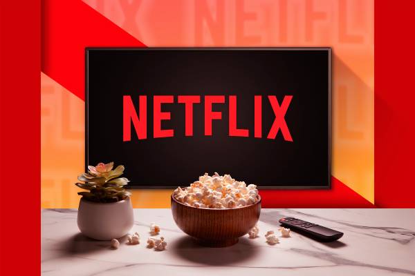 A TV with the Netflix logo, with a plant, a popcorn bowl , and a remote control on a table.