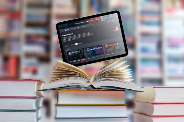 An open book with a tablet above it and a bookshelf with several books in the background.