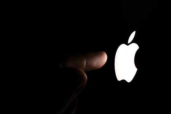 Finger pointing at glowing Apple logo in a dark.