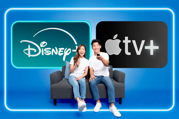 A couple sitting on a couch holding a TV remote with the Disney+ and Apple TV+ logos in the background.