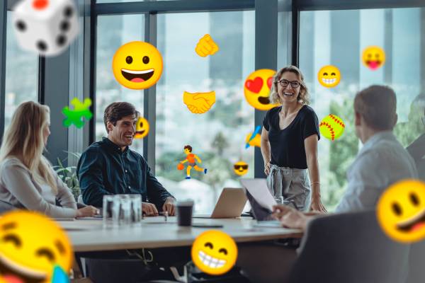 A group of people in a meeting with several emojis around them.