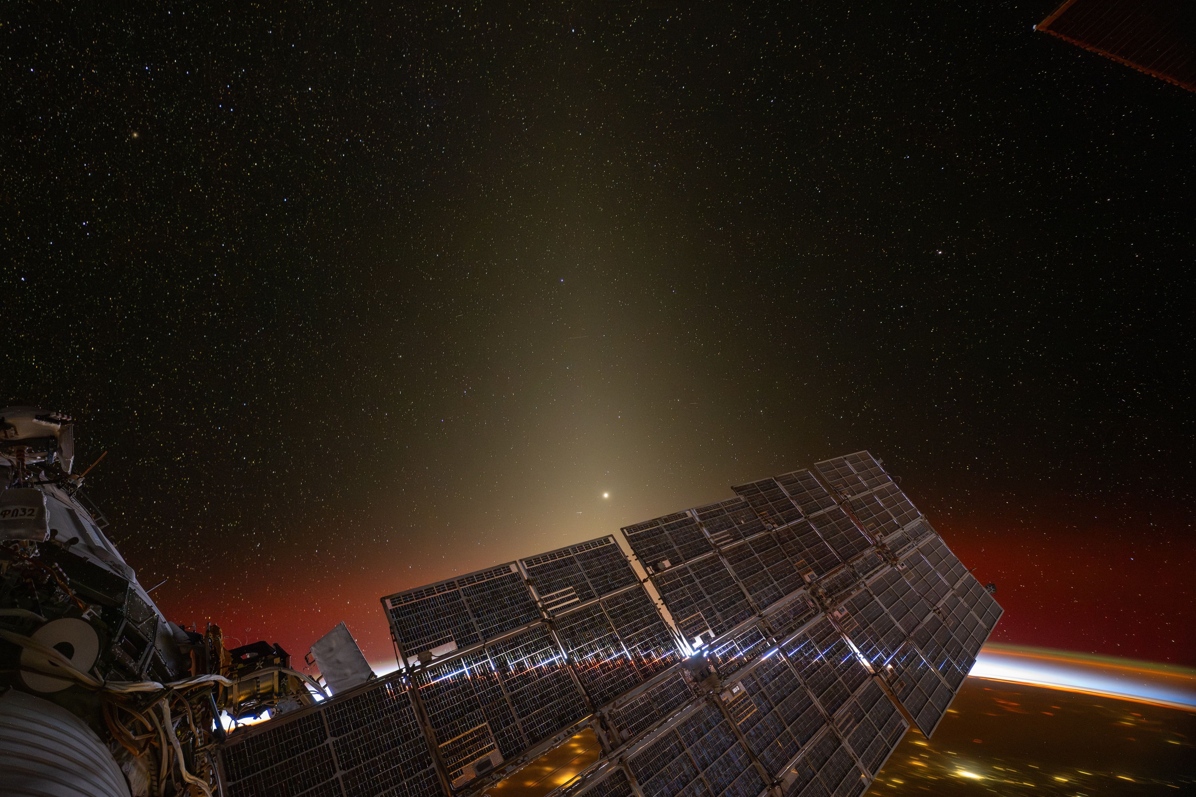 An orbital sunset shines through the service module solar arrays of the ISS.