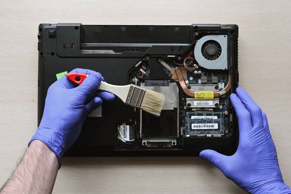 Hands with gloves cleaning the inside of an open laptop.