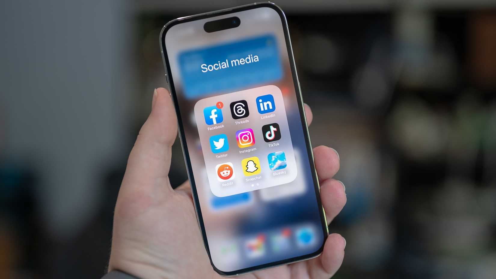 Social media folder on an Apple iPhone 14 Pro with Facebook, Threads, LinkedIn, Twitter, Instagram, TikTok, Reddit, Snapchat and Bluesky apps.