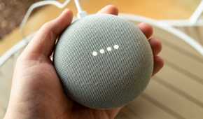 A hand holding a Google Nest speaker.