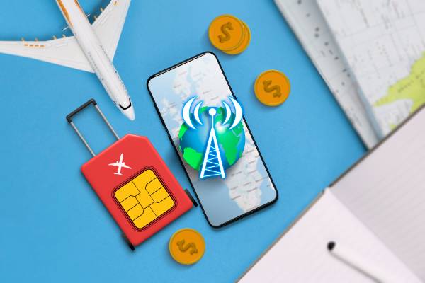 A table with a phone, a miniature airplane, a globe, a suitcase shaped like a SIM card, and some coins.