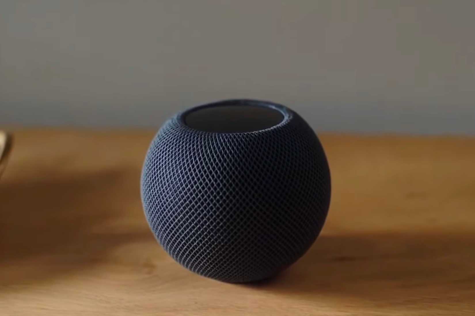 HomePod Mini preto sobre uma mesa de madeira.