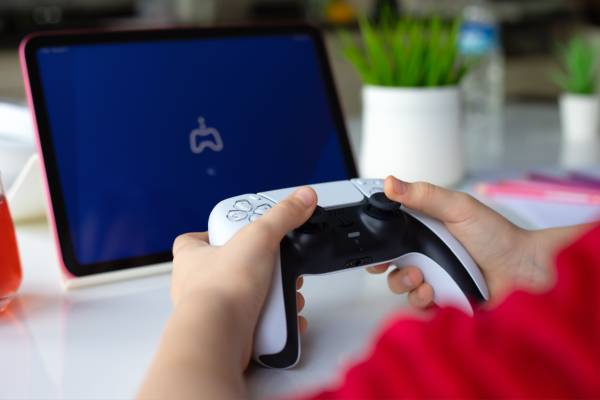 Children hands holding DualSense wireless controller Sony PlayStation 5 and Apple iPad Air.