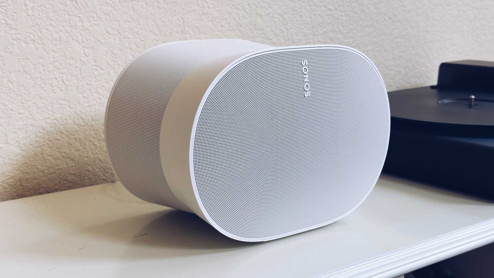 A Sonos Era 300 in white sits next to a record player on a shelf.