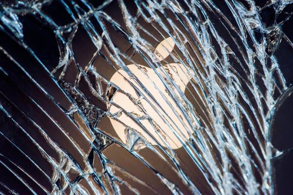 Close up of an Apple logo behind cracks on a smashed iPhone screen.