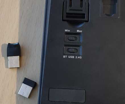 A Bluetooth / USB / 2.4G switch on the back of a keyboard along with a USB and 2.4GHz dongle.