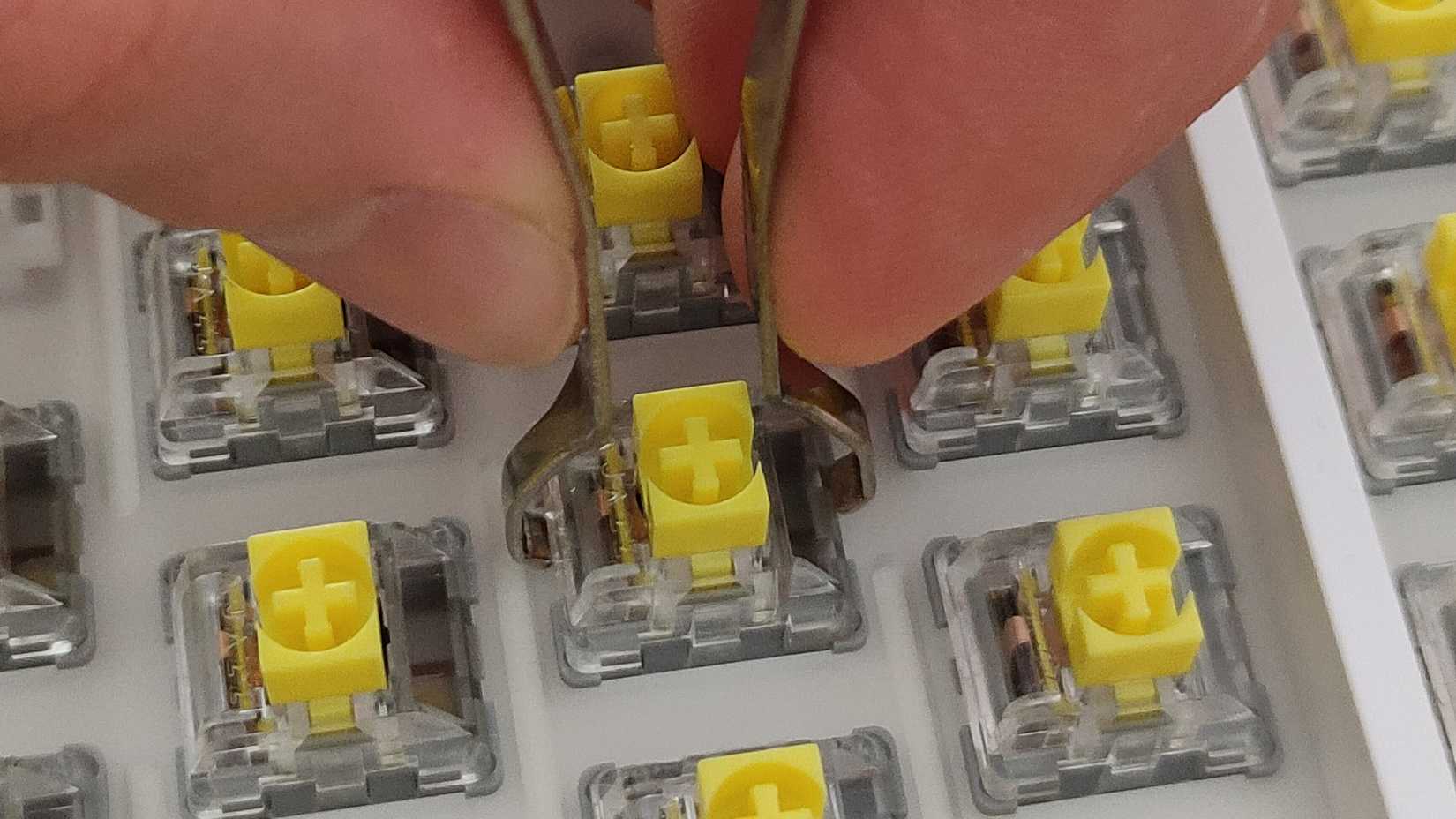 A close-up of a hand removing a mechanical keyboard switch using a switch puller.