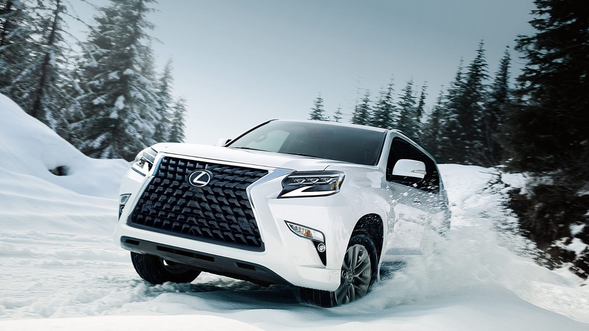 A white 2022 Lexus GX driving through the snow in a forested area.