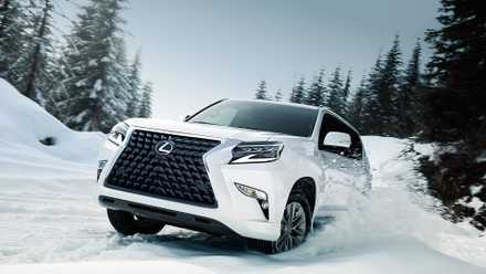 A white 2022 Lexus GX drives in the snow in a wooded area.
