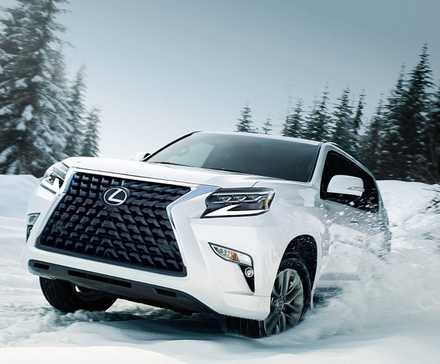 A white 2022 Lexus GX driving through the snow in a forested area.