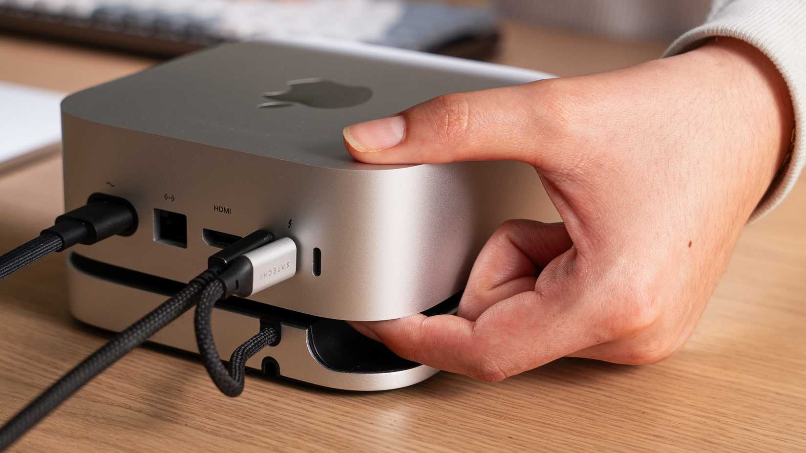 Mão alcançando o botão liga/desliga no hub Mac Mini da Satechi.