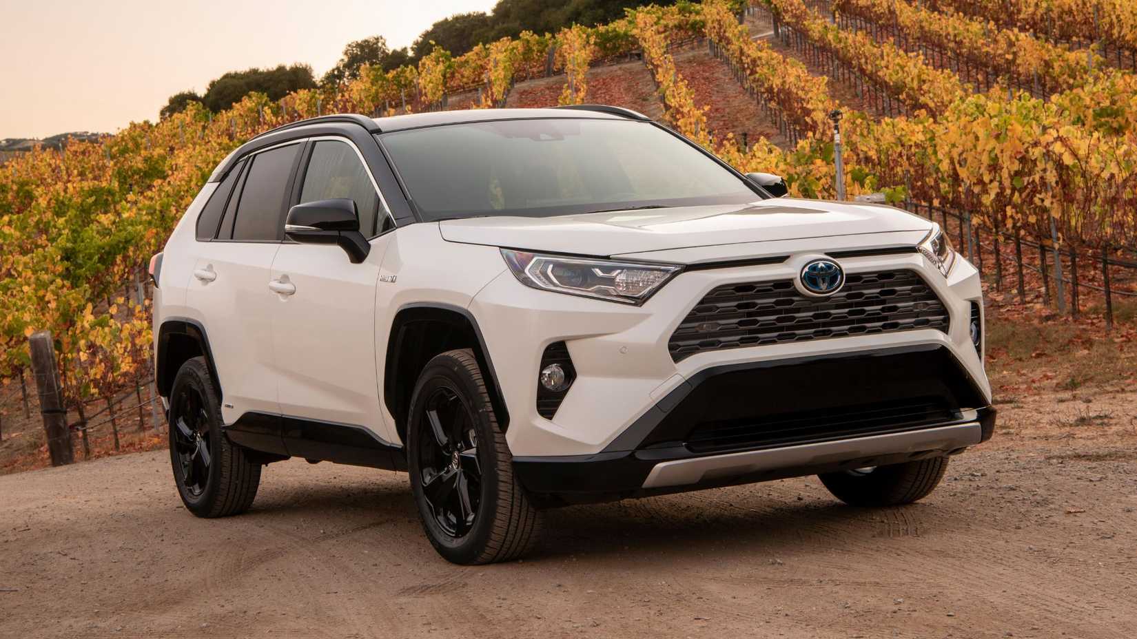Full view of white 2019 Toyota RAV4 Hybrid parked on gravel with a field in the background.