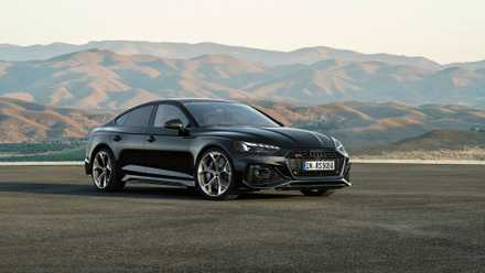 Full view of a black Audi RS5 Sportback parked on tarmac with mountains in the background.