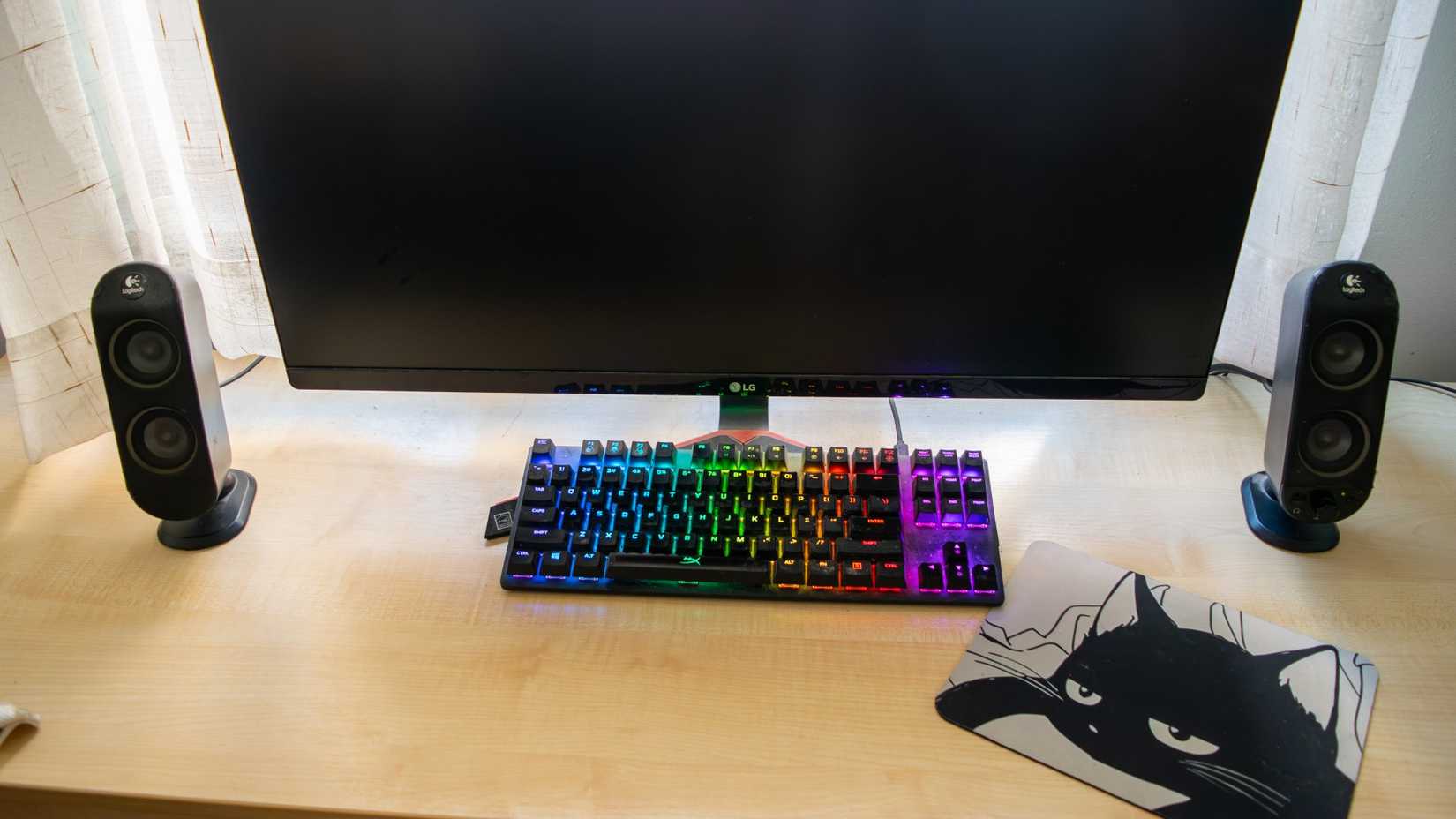 A pair of Logitech X230 speakers sitting on a table with a monitor and a keyboard between them. 