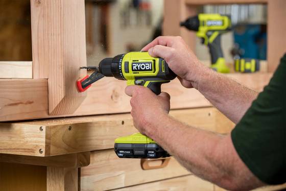 Man using a Ryobi drill on a wood deck. 