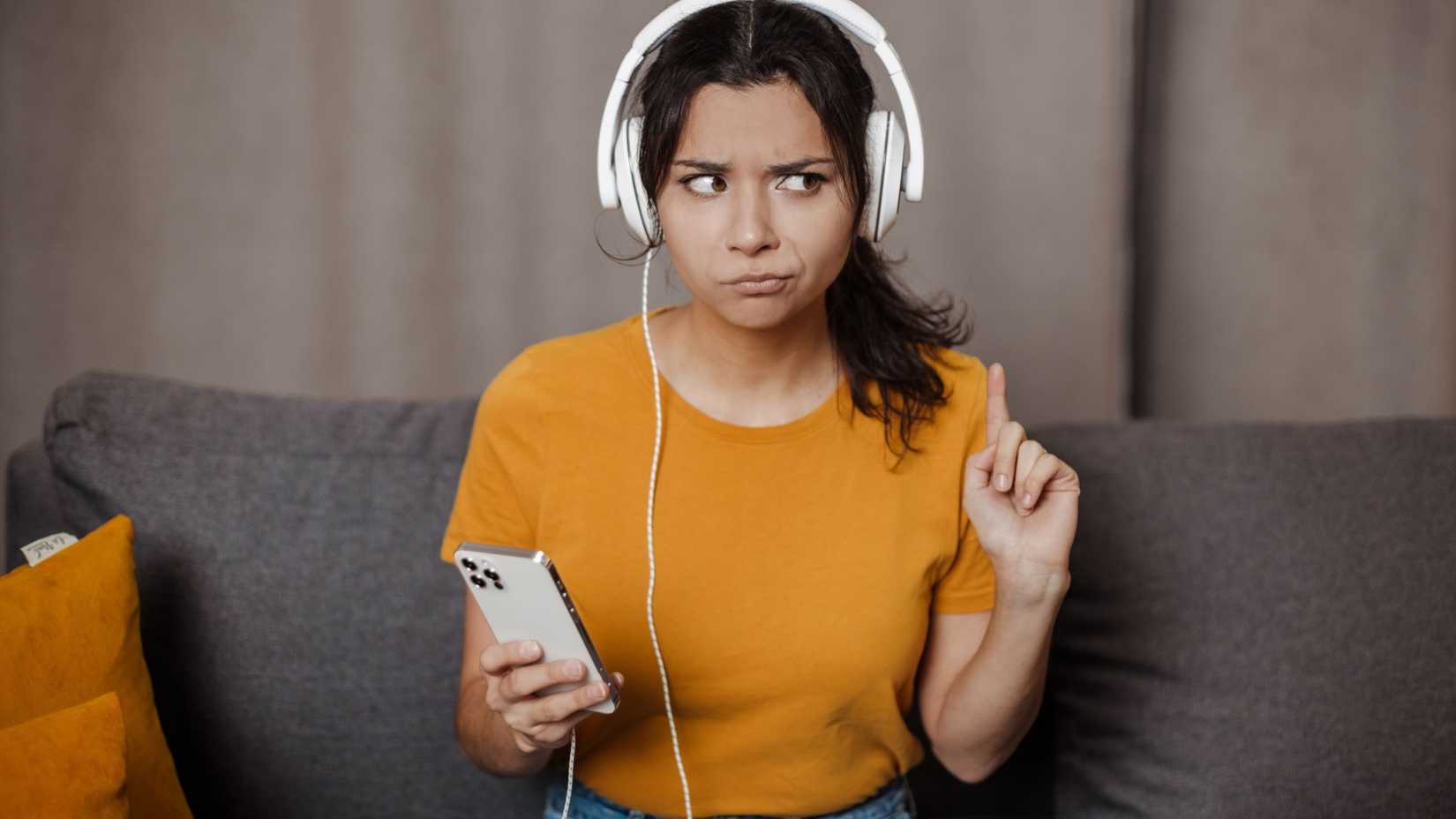 A woman listens to her iPhone with headphones and looks unhappy.