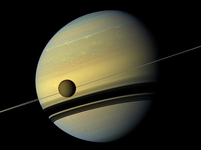 The giant moon Titan as seen from Cassini with Jupiter in the background.