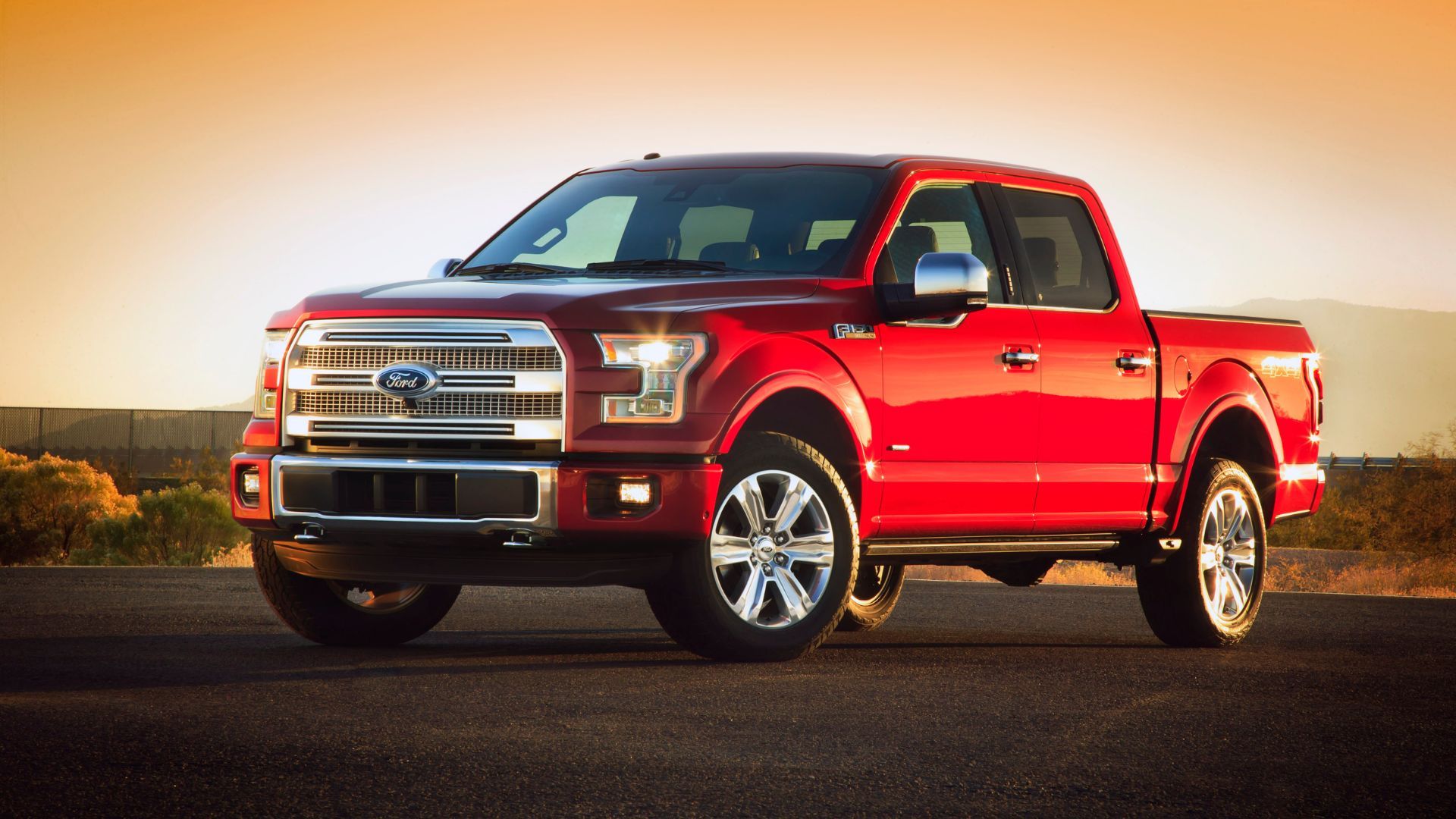 Front 3/4 view of a red 2015 Ford F-150 parked on gravel in the desert.