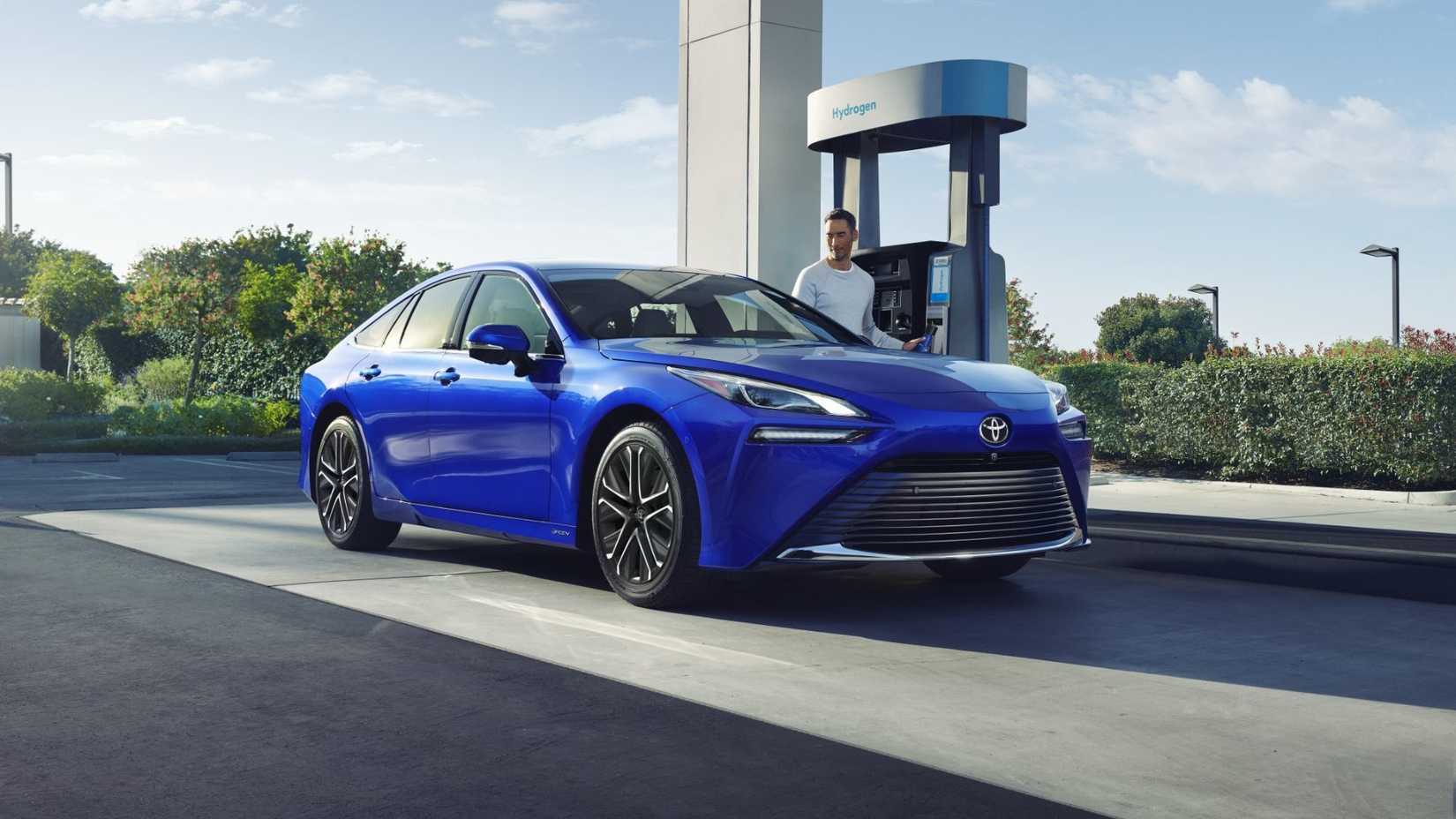Static front 3/4 shot of a blue 2024 Toyota Mirai being refueled at a hydrogen station.