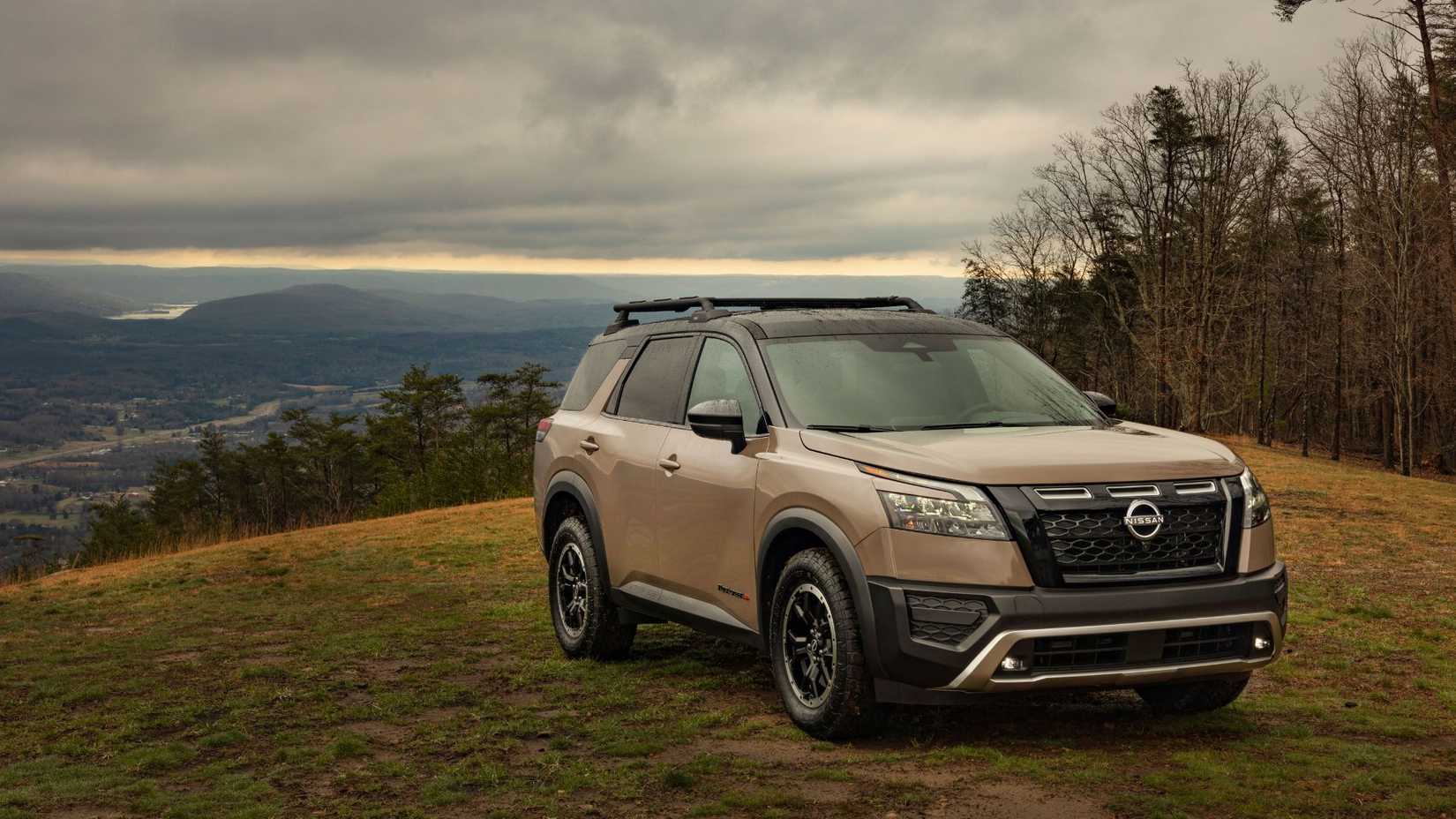 Front three-quarter view of a beige 2025 Nissan Pathfinder parked on grass in the country.
