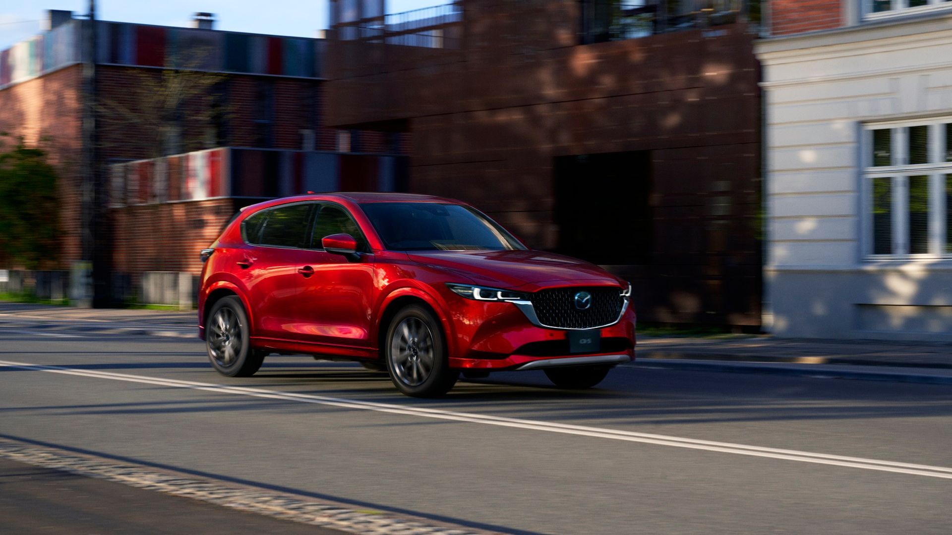 Fromt three-quarter view of a red 2025 Mazda CX-5 driving through a city.