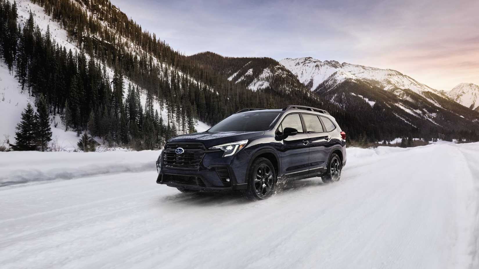 Front three-quarter view of a dark blue 2025 Subaru Ascent driving in the snow with mountains in the background.