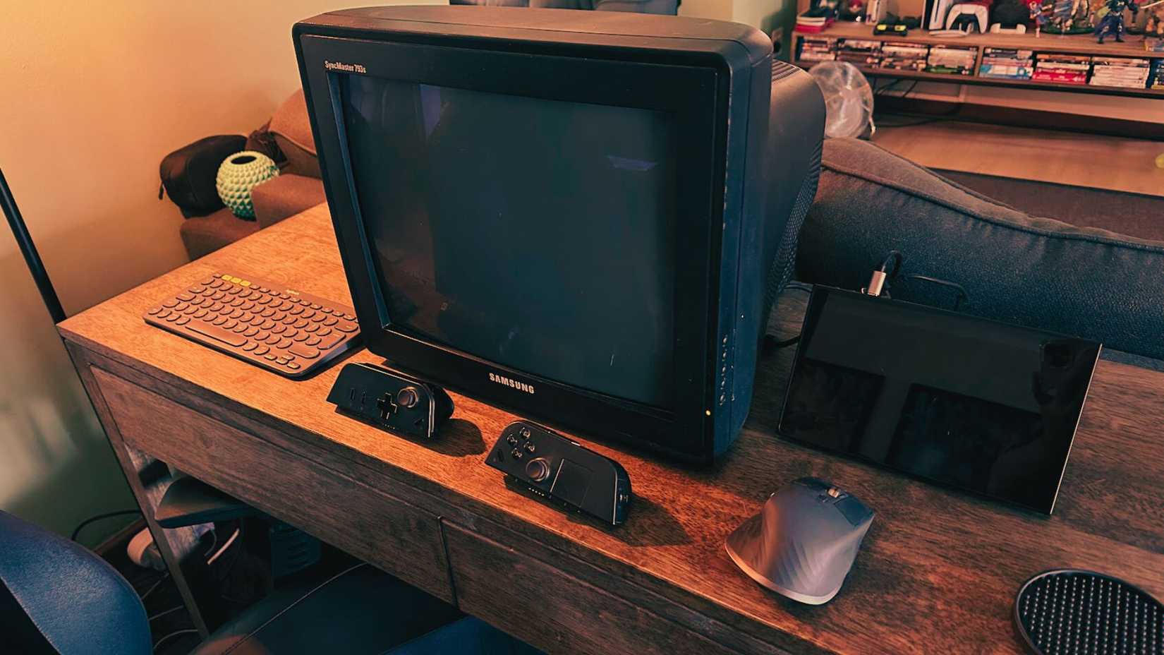 A CRT computer monitor hooked up to a handheld PC with a mouse and keyboard on a desk and some controllers.