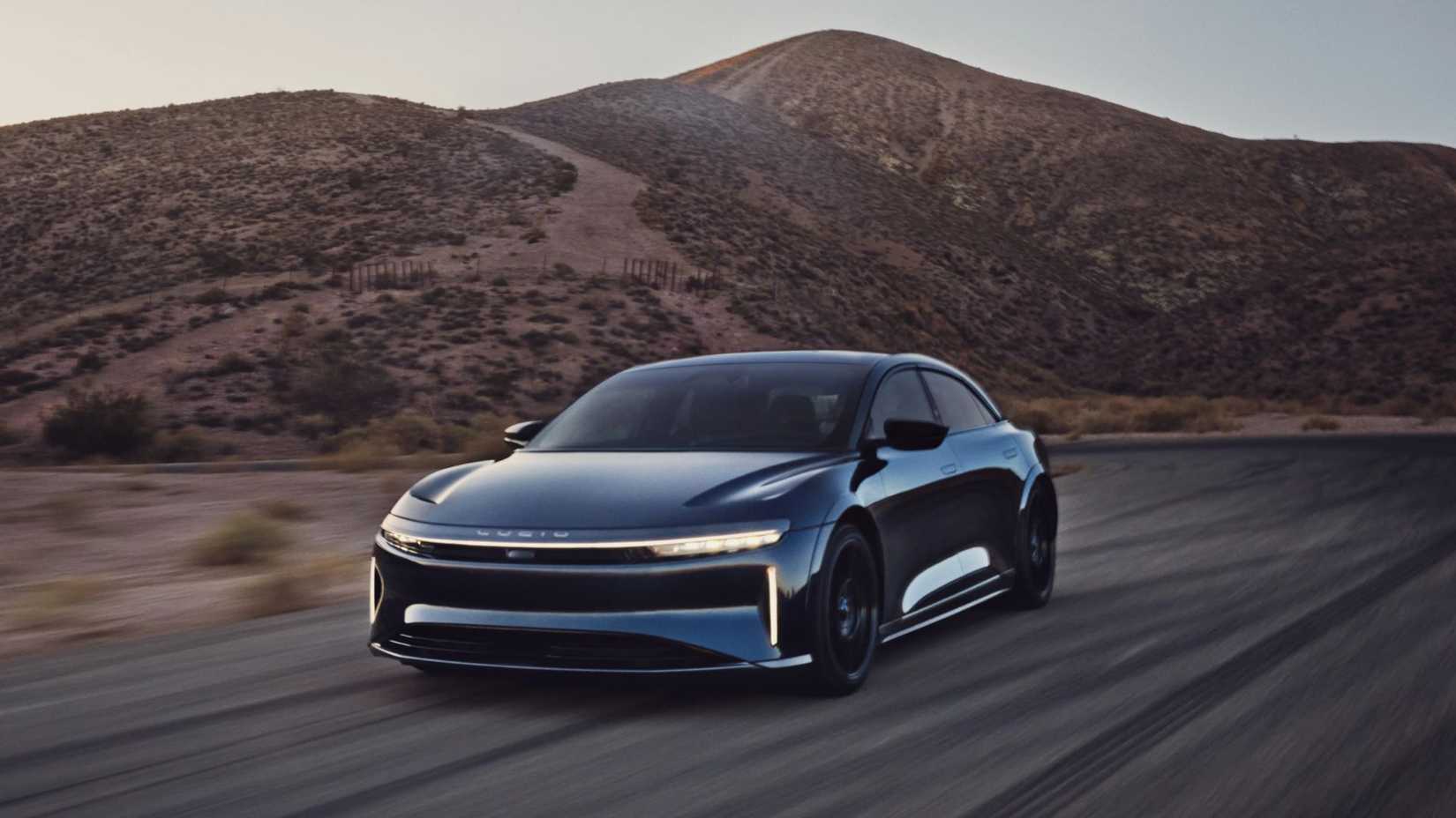 Full view of a blue Lucid Air Sapphire driving on a country road with a mountain in the background.