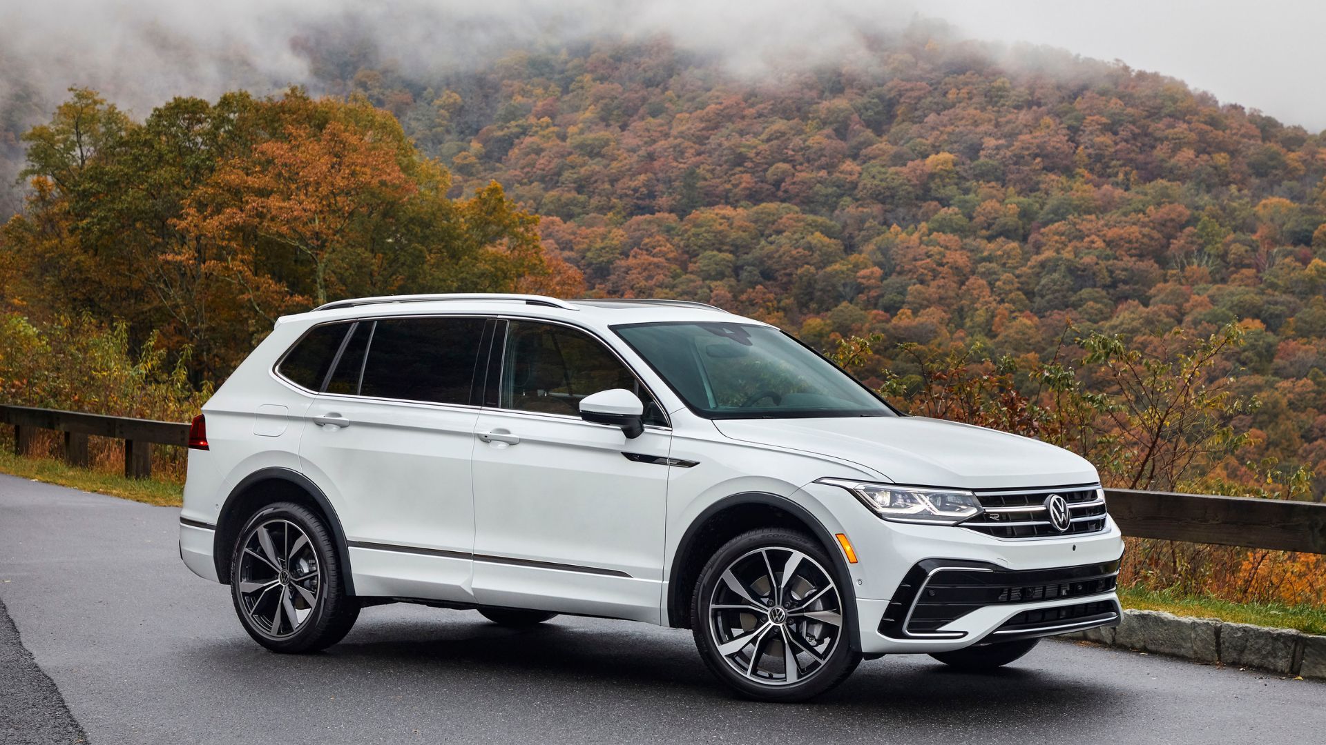 Белый Volkswagen Tiguan 2024 года выпуска, припаркованный на обочине дороги в горах, вид спереди в три четверти.