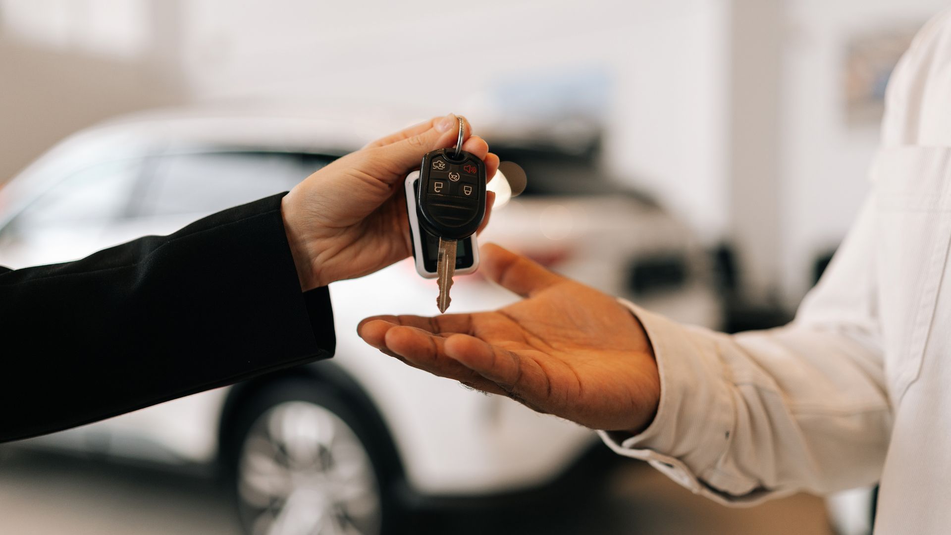 Closeup hand of unrecognizable black male buyer getting car key and greetings from auto dealer while buying new auto in dealership.