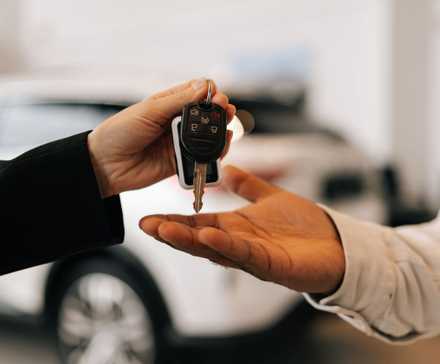 Closeup hand of unrecognizable black male buyer getting car key and greetings from auto dealer while buying new auto in dealership.