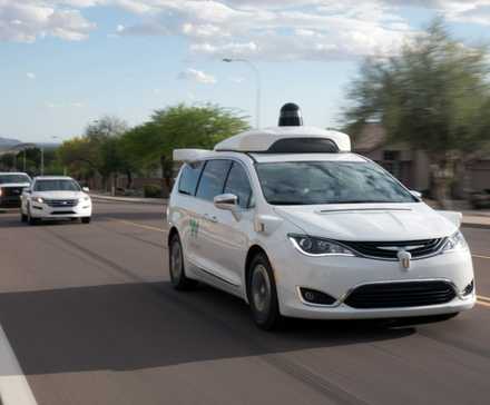 Full view of a fully autonomous Waymo Chrysler Pacifica Hybrid minivan driving on a road with vehicles following behind it.