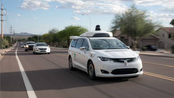 Full view of a fully autonomous Waymo Chrysler Pacifica Hybrid minivan driving on a road with vehicles following behind it.