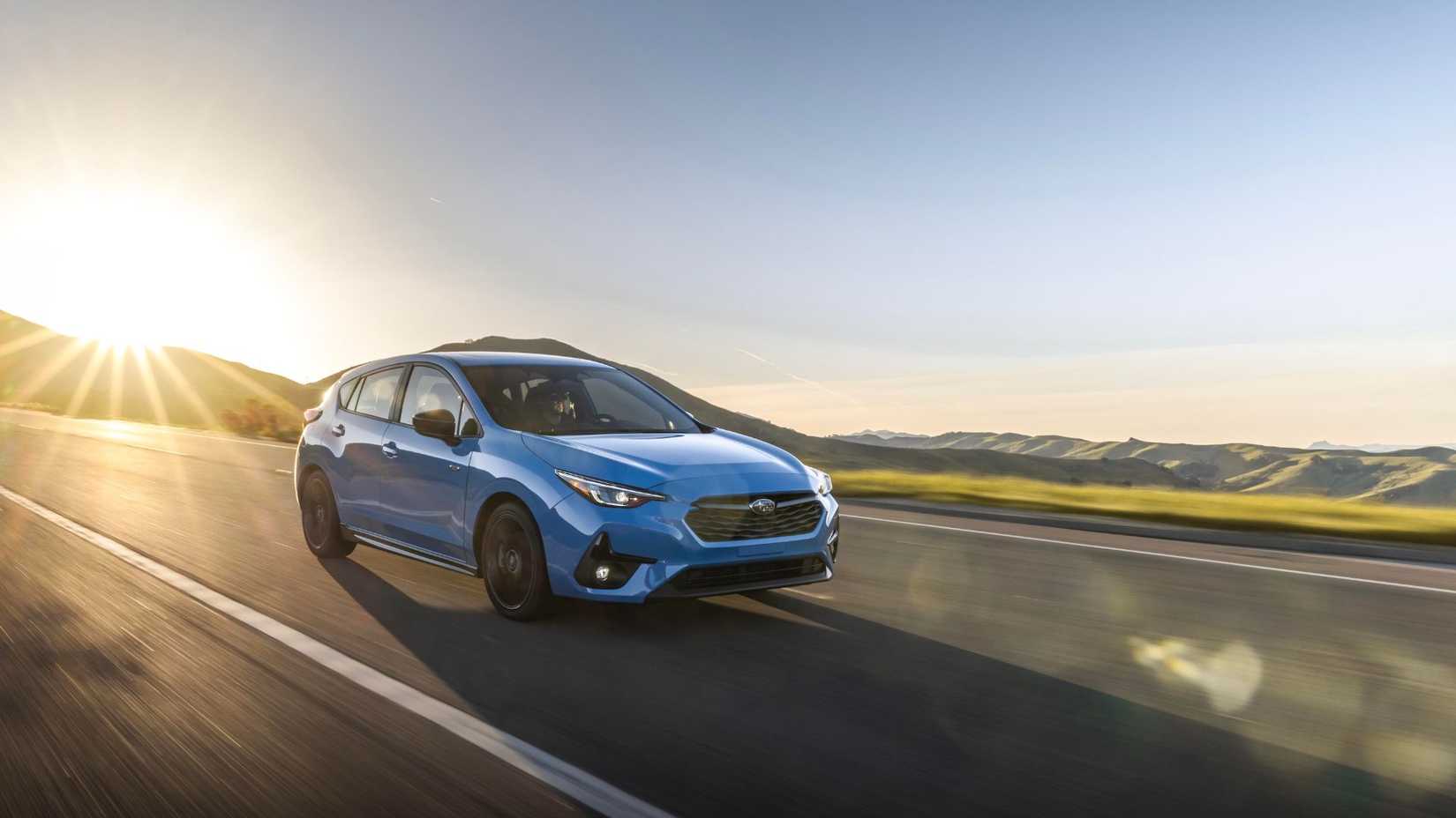 Front 3/4 view of a blue 2024 Subaru Impreza driving on a country road.