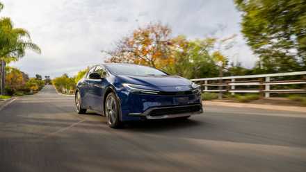 3/4 front view of a navy blue 2025 Toyota Prius driving on a country road.