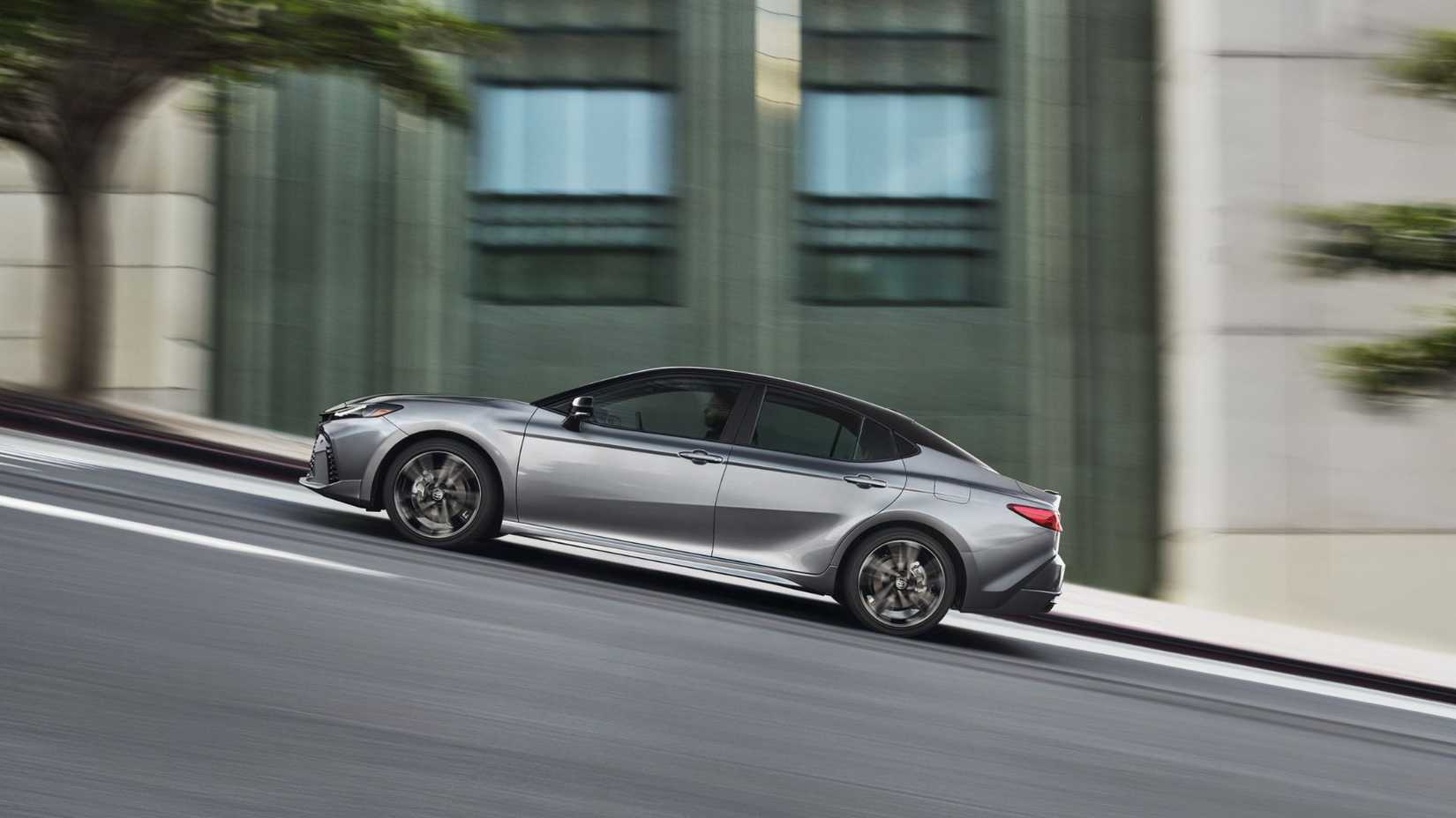Side profile shot of a gray 2025 Toyota Camry XSE driving up a hill in a city.